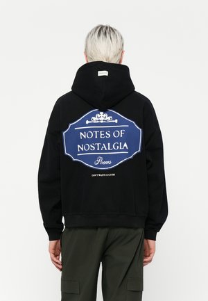 Zwarte hoodie met een groot blauw grafisch ontwerp op de achterkant, met witte tekst die luidt: "NOTES OF NOSTALGIA Gedichten" en "VERSWIND DE CULTUUR NIET."