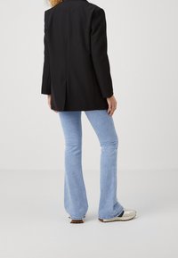 Musta muotoiltu bleiseri pitkillä hihoilla, takana halkio, yhdistetty vaaleansinisiin levennettyihin farkkuihin ja beigen värisiin tennareihin, joissa on ruskeita yksityiskohtia.