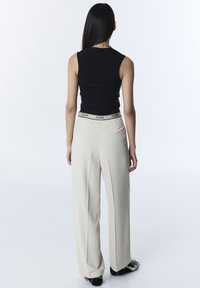 Top negro sin mangas combinado con pantalones de pierna ancha en beige claro, con una cintura elástica de marca y dos bolsillos traseros.