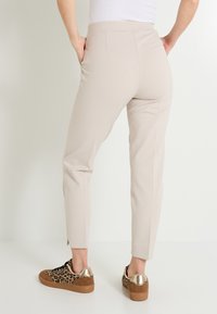 Pantalons beiges ajustés avec une texture lisse, coupe slim et poches latérales, associés à des baskets à imprimé léopard avec des accents dorés.