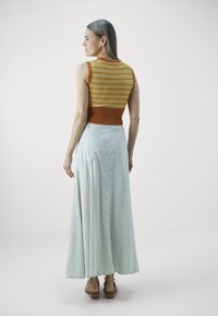Débardeur en tricot sans manches avec un bas orange côtelé et un motif géométrique jaune, associé à une longue jupe blanche et des sandales à talons bruns.