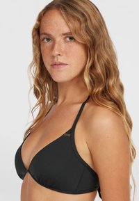 Zwarte triangulaire bikinitop met dunne banden, een soepele textuur en een klein gouden logo-detail aan de linkerkant. Eenvoudig en minimalistisch ontwerp.