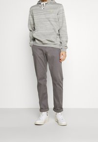 Felpa a righe grigie chiare con cordini, tasca frontale; abbinata a pantaloni grigi scuri e sneakers bianche, con risvolti.