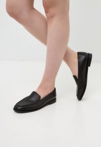 Black leather loafers with a pointed toe design and low heel, featuring a smooth texture and minimalistic style.