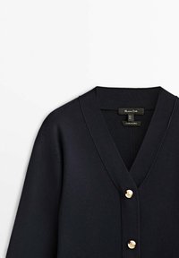 Cardigan marine en tissu doux et texturé, avec un décolleté en V et trois accents en bouton doré sur la fermeture avant.