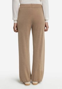 Brede beige broek gemaakt van een zachte, gestructureerde stof. Heeft een elastische tailleband en een ontspannen pasvorm, die tot de grond reikt.