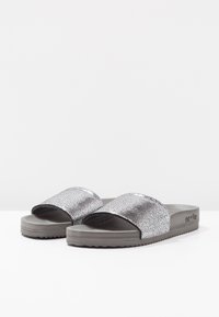 Silver textured slide sandals featuring a wide band and a gray rubber sole with a treaded design. Branding visible on the side.