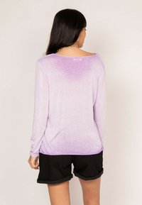 Haut à manches longues lavande avec un dégradé de couleur claire à foncée, présentant une coupe décontractée et une texture douce, associé à un short noir.