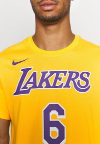 Żółta bawełniana koszulka z napisem "LAKERS" w fioletowych literach oraz numerem 6, z fioletowym logo Nike na lewym ramieniu.
