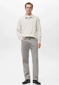 Polo shirt grigio chiaro, maniche lunghe, tessuto leggero; abbinato a jeans dritti grigio chiaro; il modello indossa scarpe nere.