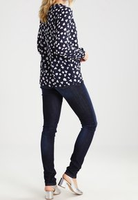 Navy blouse with white floral pattern, long sleeves, paired with dark jeans and silver heeled mules, showcasing a casual outfit.