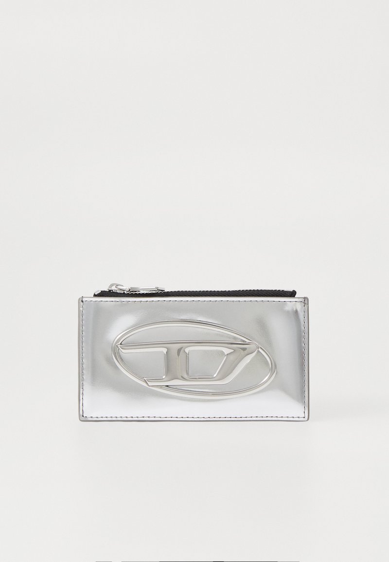 Silver metallic wallet with a smooth texture and a prominent logo detail. Features a zip closure and rectangular shape.