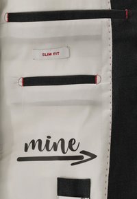 Das Innenfutter der Slim-Fit-Jacke besteht aus weißem Stoff mit roter Naht, zwei schwarzen Stofftaschen, einem Etikett und dem in Schwarz aufgedruckten Wort "mine".