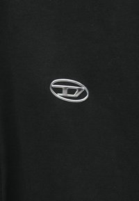 Μαύρο βαμβακερό t-shirt με ασημένιο λογότυπο σε σχήμα οβάλ στο μπροστινό μέρος. Το ύφασμα φαίνεται λείο με μια διακριτική υφή.