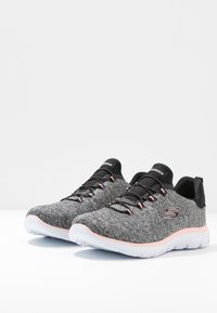 Grey knit athletic shoes with black accents, pink laces, and a white cushioned sole. Features a logo and breathable upper design.