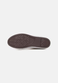 Σόλα ενός λευκού αθλητικού παπουτσιού Converse All Star που εμφανίζει καστανόσκούρο ελαστικό πέλμα με σχέδια αστεριού και ρόμβου καθώς και το λογότυπο της μάρκας.