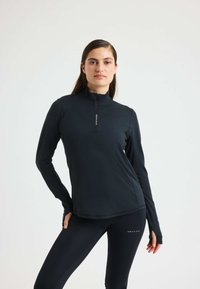 Camiseta deportiva negra de manga larga con cuello alto y cierre de media cremallera, que presenta una textura suave y un detalle de logo en la parte delantera.