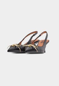 Μαύρα γόβες slingback από δερμάτινη λουστρίνι με μυτερά δάχ τυλα, μπεζ φιόγκους και μικρά χρυσά κρεμαστά διακοσμητικά σε σχήμα καρδιάς σε λευκό φόντο.
