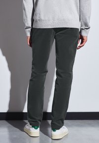 Pantalones de pana verde oscuro con corte ajustado y sutil textura acanalada, combinados con zapatillas blancas con acentos verdes.