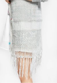 Hellblauer, gestrickter Überwurf mit strukturierten Streifen und dekorativen Fransen am Saum. Hergestellt aus einem weichen Material mit filigranen Mustern.