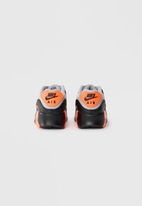 Nike Air tenisky s šedou síťovinou, oranžovými akcenty a černou gumovou podrážkou; mají značkování na patě a strukturované povrchy.