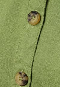 Groene linnen stof met twee ronde, bruine en beige knopen, met een gestructureerd oppervlak en zichtbare stiksels langs de knoopsluiting.