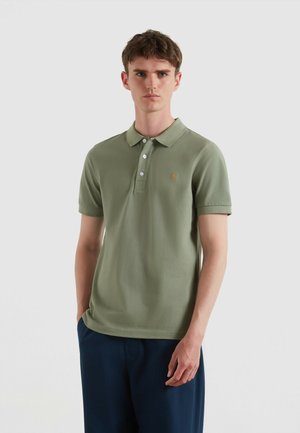 Polo olive vert à manches courtes, avec une patte de boutonnage à trois boutons et un accent brodé. Tissu lisse offrant une coupe classique, associé à un pantalon bleu marine.