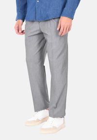 Pantaloni grigi da abito con un sottile motivo a righe, dal taglio su misura, abbinati a sneakers bianche. Il tessuto ha una consistenza liscia.