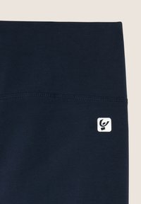 Leggings blu navy realizzati in tessuto elastico, con una superficie liscia e un piccolo logo bianco sulla cintura.