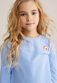 Camisa de manga larga azul claro hecha de tela suave que presenta un diseño de arcoíris multicolor con un corazón y detalles florales en el pecho.