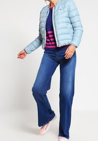 Ljusblå pufferjacka med en figurnära design, kombinerad med en marinblå och röd randig tröja samt utsvängda blå jeans, kompletterad med rosa sneakers.