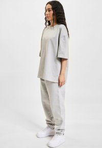Light gray oversized t-shirt with short sleeves paired with matching tapered sweatpants and white sneakers. Smooth fabric, simple design.