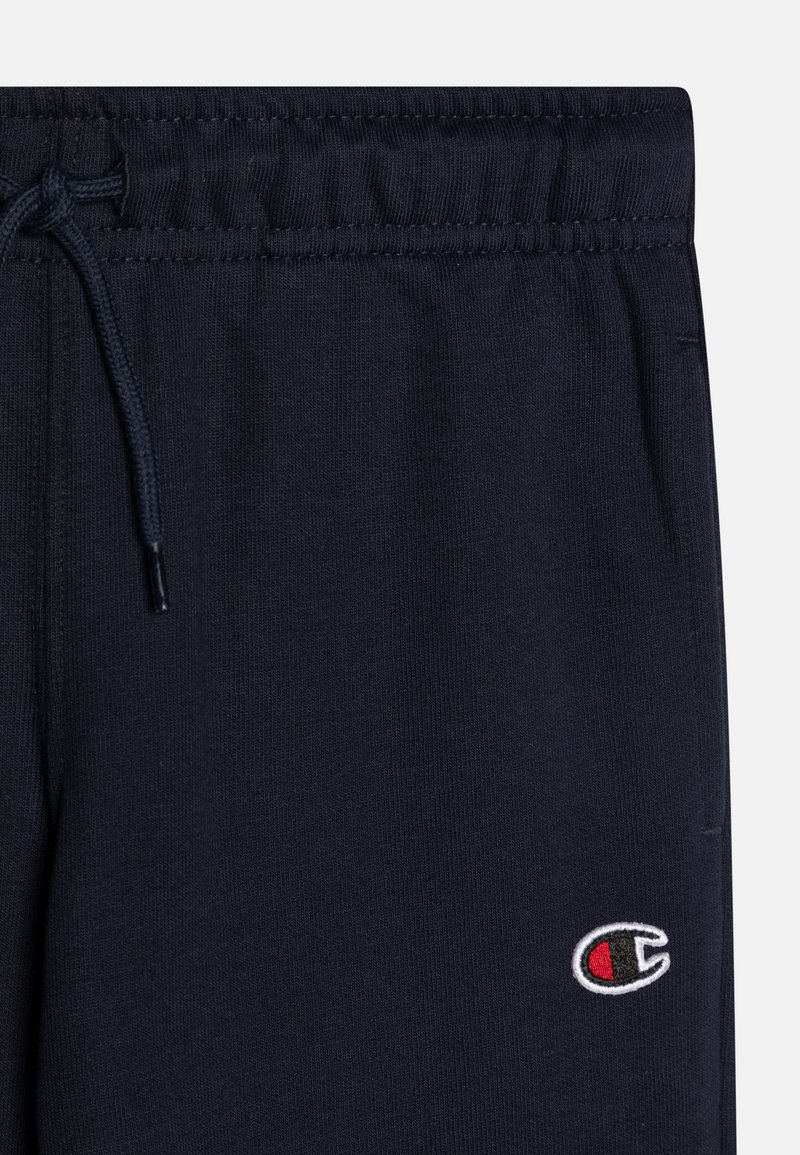 Pantalons de survêtement bleu marine avec une taille à cordon, présentant un petit logo brodé en rouge et blanc sur la jambe gauche, fabriqués en tissu doux.