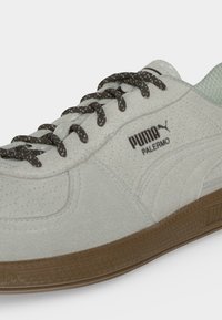 Κοντινό πλάνο ανοιχτόγκρι αθλητικού Puma Palermo με σκούρα γκρι κορδόνια και καφέ λαστιχένια σόλα σε λευκό φόντο.