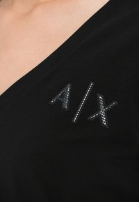 Juoda V-kaklo marškinėliai su tekstūruotu „A/X“ logotipu tamsiai pilkos spalvos, su karoliukais kairėje pusėje. Minkšta medžiaga su lygia apdaila.