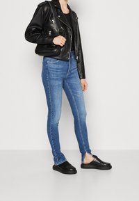 Black leather biker jacket over a black top, paired with light blue skinny jeans and black slip-on shoes. Noticeable side slits on jeans.