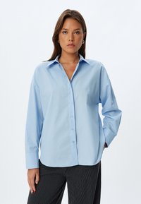 Camicia button-up azzurro chiaro realizzata in tessuto morbido, con colletto classico, maniche lunghe e vestibilità rilassata. Senza motivi visibili.