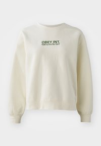 Light cream sweatshirt made of soft fabric. Features a green "OBEY INT." logo above city names. Comfortable fit with ribbed cuffs.