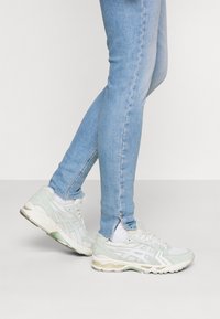 Zapatillas deportivas de color verde claro con materiales de malla y ante, que cuentan con acentos blancos, una suela acolchada y un collarín acolchado.