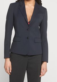 Blazer bleu marine avec une coupe ajustée, deux poches avant et une fermeture à boutons. Confectionné en tissu lisse avec une silhouette moderne et cintrée.