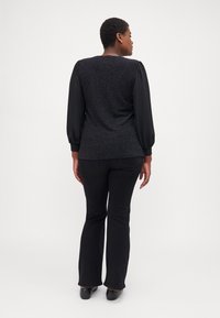 Black flared pants with a smooth texture, paired with a dark top featuring patterned fabric and long, puffed sleeves.