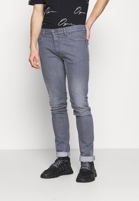 Smal passform på grå denimjeans med en något blekt finish, bältesöglor, framfickor och uppvikta benslut. Bärs med svarta sportskor.