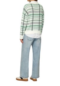 Lässig sitzender, hellgrüner und weiß gestreifter Pullover mit schwarzen Linien, kombiniert mit lockeren blauen Jeans und beigen Sneakern.