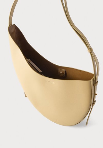 Μπεζ δερμάτινη τσάντα ώμου με ρυθμιζόμενο λουράκι, ανοιχτό πάνω μέρος, εσωτερική τσέπη με φερμουάρ και μαγνητικό κούμπωμα.