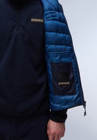 Granatowy polar z ćwierć zamkiem, z niebieskim rękawem z puchowej kurtki oraz kieszeniami na naszywkę z logo wewnątrz i detalami na mankietach.