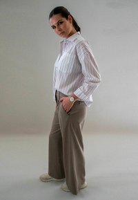 Gestreepte button-up shirt in wit en lichtroze, gecombineerd met beige wijde broek. Geaccessoriseerd met een gouden horloge en lichte sneakers.