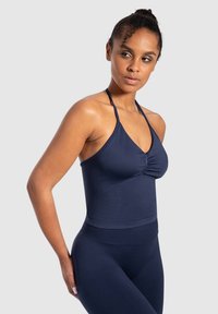 Navyblauwe haltertop met een gerimpelde voorkant, naadloos ontwerp en een aansluitende band bij de taille, gecombineerd met bijpassende leggings.
