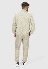 Hellgraue Jacke mit geometrischem Muster, elastischen Bündchen und hohem Kragen, kombiniert mit passenden Hosen und weißen Turnschuhen.