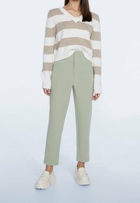 Pull en maille beige et blanche à rayures avec un col en V, associé à un pantalon sur mesure vert clair. Le modèle porte des mocassins à plateforme crème.