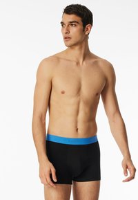 Black boxer briefs with a blue waistband, made of soft fabric. The waistband features the brand name in a subtle design.